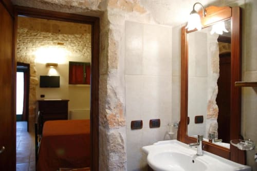 Bagno moderno con piastrelle bianche, specchio con cornice in legno e lavabo nell'appartamento Trulli Boccadoro