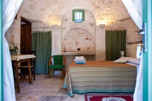 Camera da letto in trullo con volte in pietra, coperta rigata, sedie verdi e arredamento tradizionale della campagna italiana