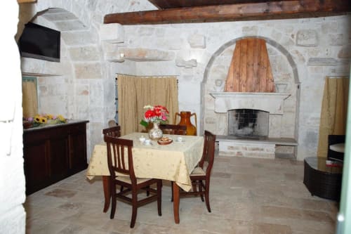 Interno tradizionale di trullo con muri in pietra, camino, mobili in legno e tavolo da pranzo presso Trulli Boccadoro B&B
