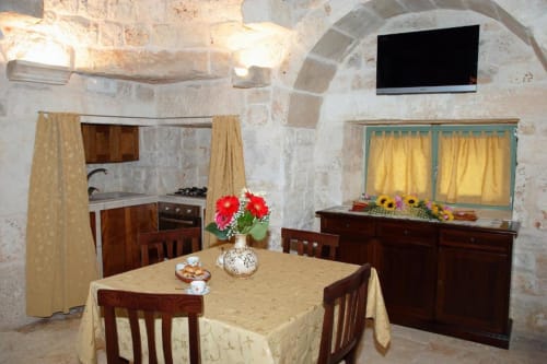 Area pranzo dello studio Trulli Boccadoro con archi in pietra, mobili in legno e angolo cottura attrezzato