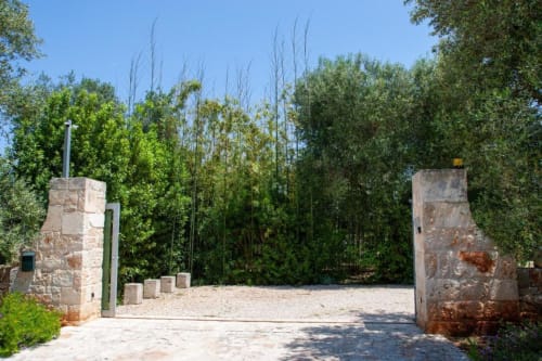Ingresso in pietra della Trulli Boccadoro con alti pioppi e rigogliosi giardini, Puglia Italia