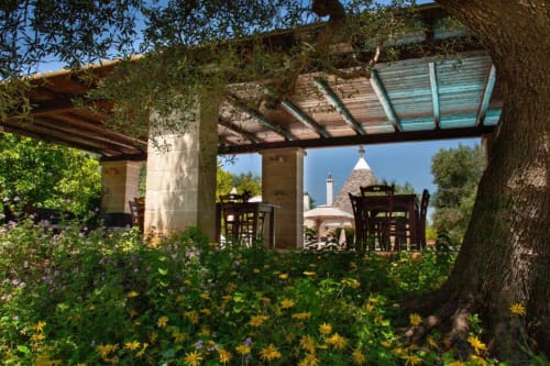 Area ristorazione all'aperto presso Trulli Boccadoro con pergolato, fiori gialli e tradizionale architettura trullo in Puglia,