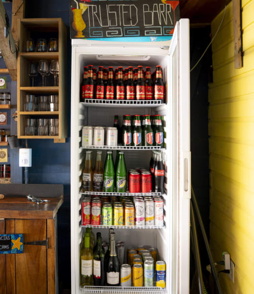 Refrigerator stocked with beverages at BarrBra BnB in Bocas del Toro, displaying beer, soda, and wine bottles on wire