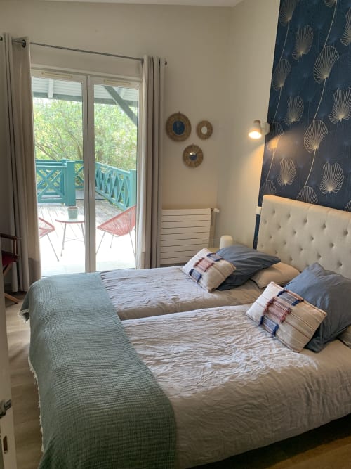 Modern bedroom with two beds, blue patterned headboard, and French doors opening to a garden terrace with mountain views at