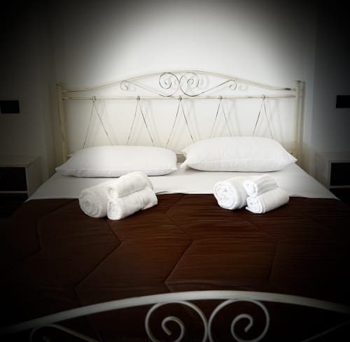 Elegantly prepared double bed with white pillows and rolled towels at B&B Hélios in Nardò