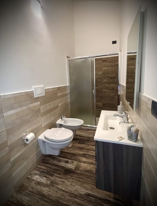 Bagno moderno presso il B&B Hélios a Nardò con doccia a filo pavimento, bidet, lavabo e rivestimento in gres effetto legno