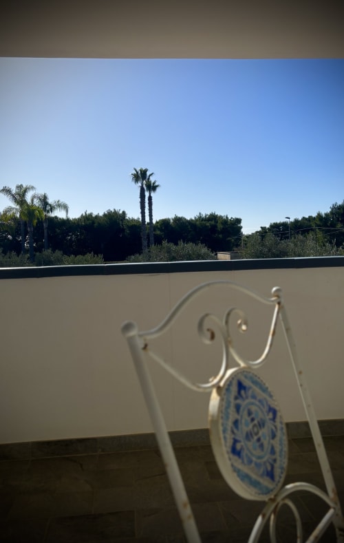 Sedia bianca ornamentale con dettaglio in ceramica blu che affaccia su palme e giardini della B&B Hélios, Nardò Italia