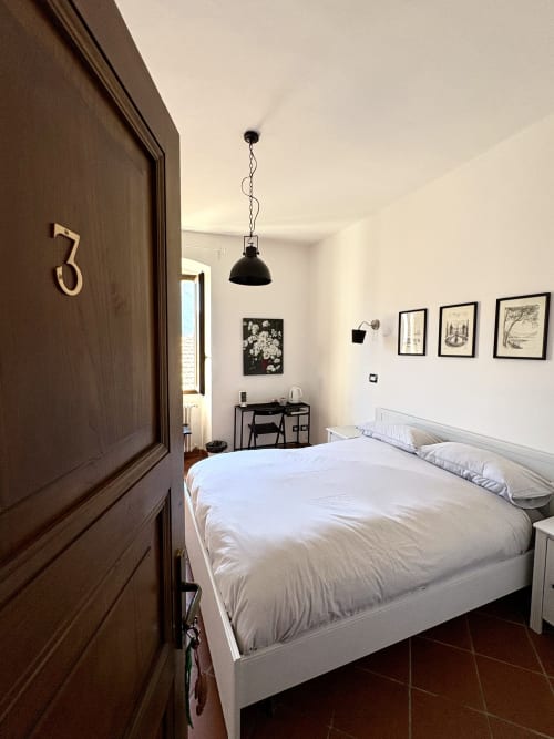 Camera tripla a La Dolce Casa B&B a Cremia con letto bianco, porta in legno scuro, lampada a sospensione e vista sul giardino
