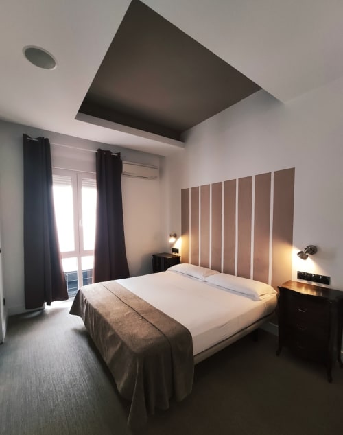Dormitorio moderno del Hostal Santa Ana Colors en Madrid con cama de matrimonio, panel de techo oscuro y cabecero con detalles de rayas