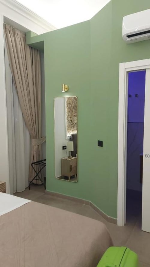 Modern bedroom at Pignasecca Domus Naples with mint green walls, mirror, beige curtains, blue door, AC unit
