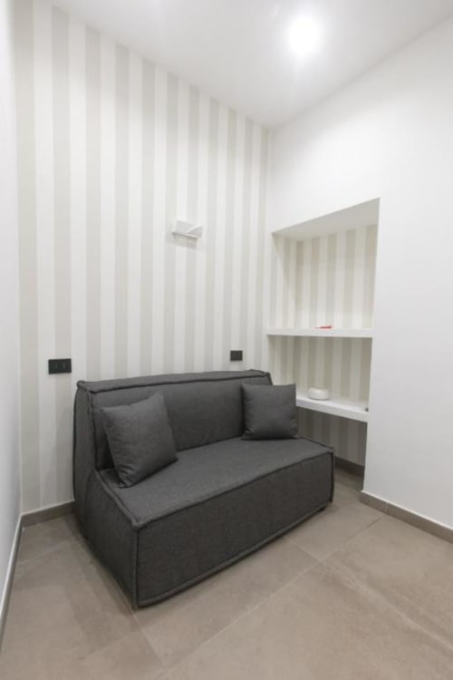 Modern guest room at Pignasecca Domus Naples with gray sofa, striped wallpaper, and built-in shelving