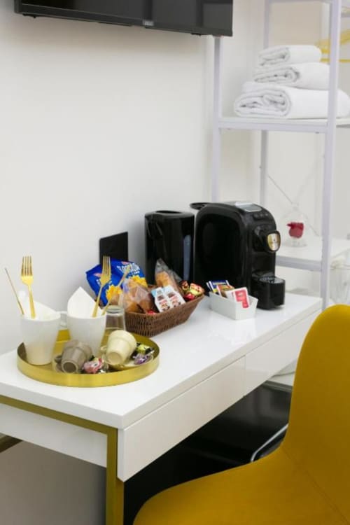 Hotel room amenities at Pignasecca Domus Naples: desk with coffee maker, snacks, toiletries, and white towels on shelf