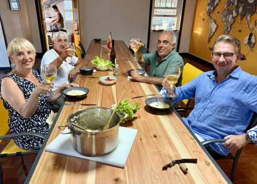 Four guests enjoying dinner with wine at Golden Mermaid Villa's wooden table in Portugal, yellow walls visible.