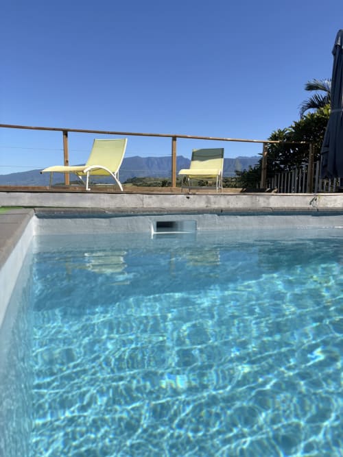 Piscine cristalline à l'Hôtel le soleil couchant à Saint-Pierre avec transats jaunes et vue sur les montagnes