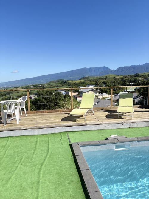 Terrasse piscine de l'Hôtel le soleil couchant à Saint-Pierre, Réunion, avec chaises longues, terrasse en bois et vue sur les montagnes