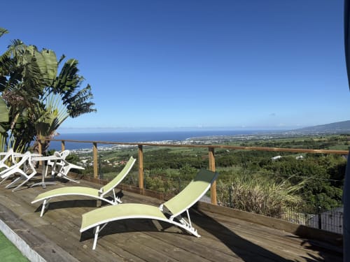 Terrasse avec vue sur l'océan à l'Hôtel le soleil couchant, chaises longues face à Saint-Pierre, côte de la Réunion et paysage luxuriant