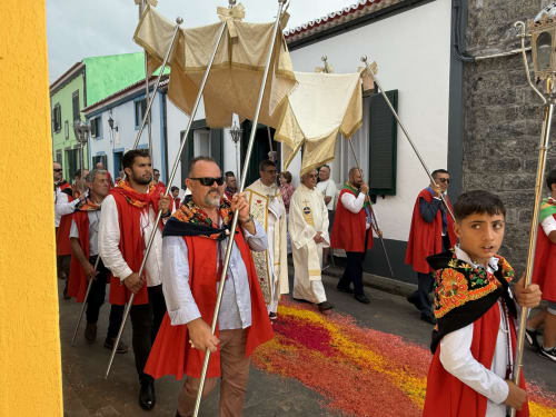 Religious procession at Golden Mermaid Villa with participants in red robes carrying canopies down colorful flower-strewn
