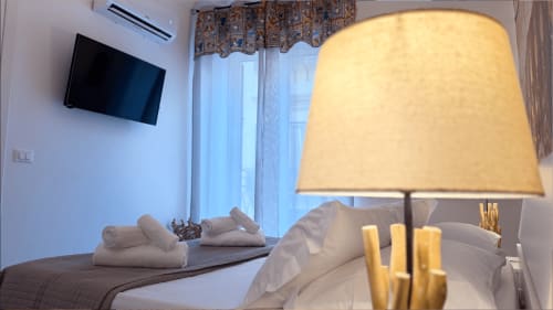 Camera da letto elegante a Palermo con biancheria crema, asciugamani arrotolati, lampada da tavolo calda e TV a schermo piatto