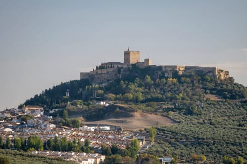 Castillo medieval encaramado en la cima de una colina sobre el pueblo de Castillo de Locubín, con olivares y arquitectura tradicional en las laderas