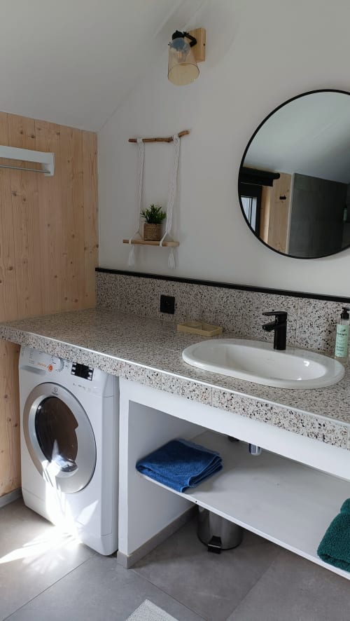 Salle de bain moderne avec lave-linge à la clef des bois à Paliseul, comptoirs en terrazzo et miroir rond
