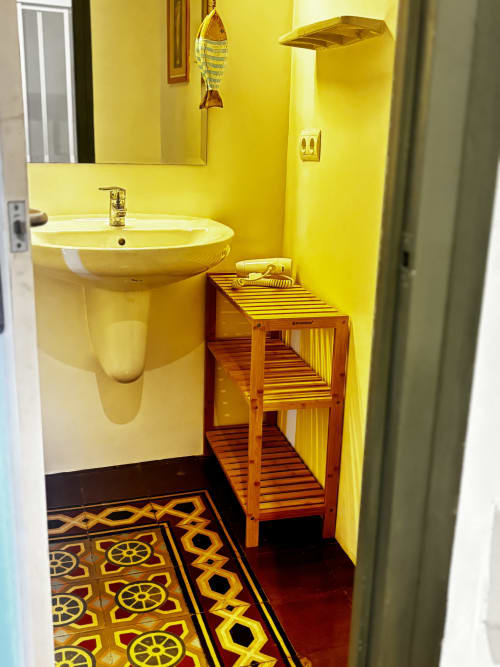 Bright yellow bathroom with pedestal sink, wooden shelving, and nautical-themed floor at Mas Ribas Hotel in Palamos