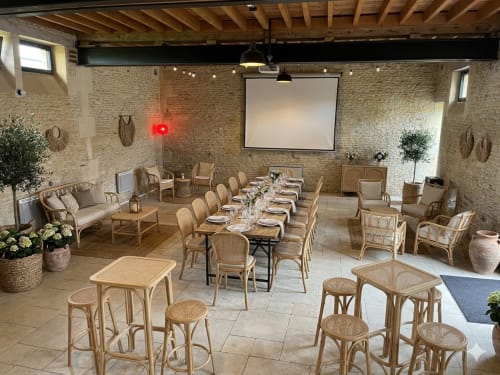 Salle à manger élégante au Domaine Du Grand Fort avec table longue, chaises en rotin, briques apparentes et écran de projection pour événements