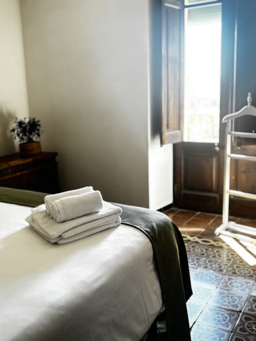 Modern bedroom at Mas Ribas Hotel in Palamos with neatly stacked towels on bed, garden view, and patterned tile flooring