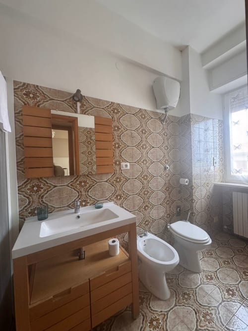Baño moderno en B&B Residenza Leonardo, Falconara Marittima, con mueble de madera, bidé, inodoro y paredes con azulejos decorativos