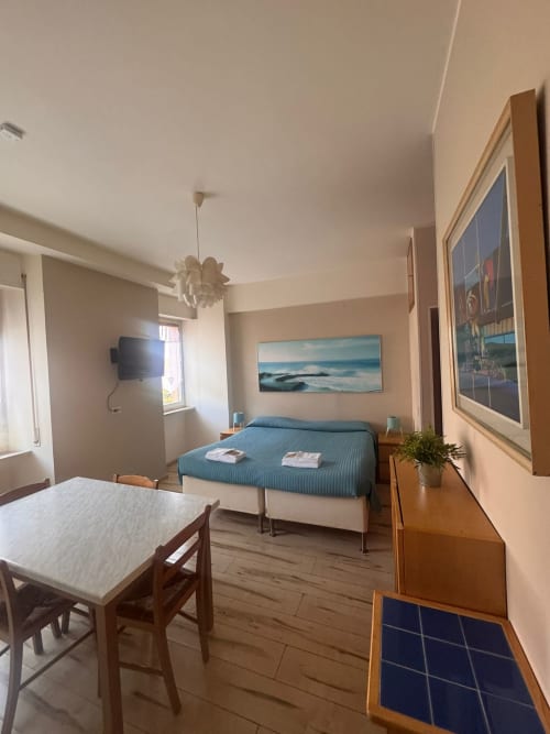Moderno dormitorio estudio con sofá cama azul, mesa comedor, cuadro de vista al mar y TV de pantalla plana en B&B Residenza Leonardo
