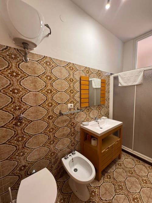 Baño moderno con azulejos decorativos beige, mueble de madera, bidé e inodoro en B&B Residenza Leonardo, Falconara Marittima