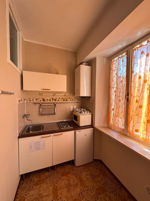 Pequeña cocina en B&B Residenza Leonardo, Falconara Marittima con estufa, fregadero, refrigerador y ventana con naranja