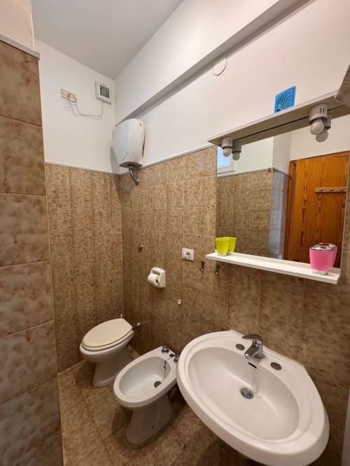 Baño limpio con azulejos marrones, lavabo blanco, bidé, inodoro y espejo en B&B Residenza Leonardo, Falconara Marittima
