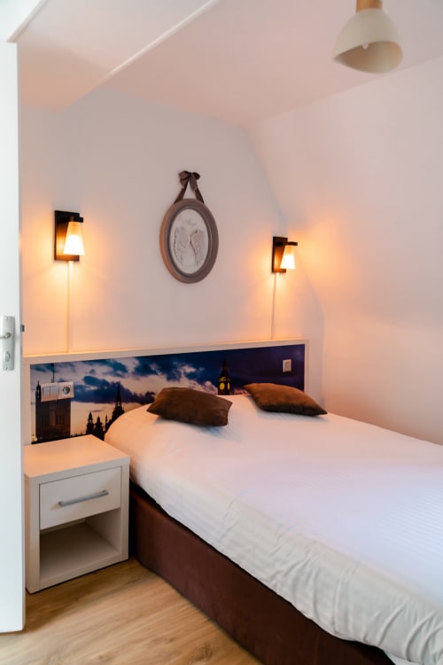 Chambre double moderne à l'Hôtel les Initiés à Rouen avec éclairage mural ambiant, tête de lit vue sur la ville et plafond mansardé
