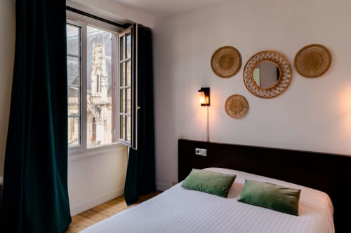 Chambre moderne à l'Hôtel les Initiés à Rouen avec lit double, oreillers verts, décoration murale tressée, rideaux noirs et fenêtre