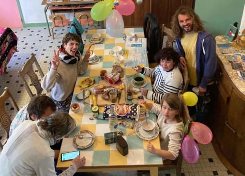 Family enjoying meal at Le Lama Zébré guesthouse in Penmarch, France with festive balloons and checkerboard table.