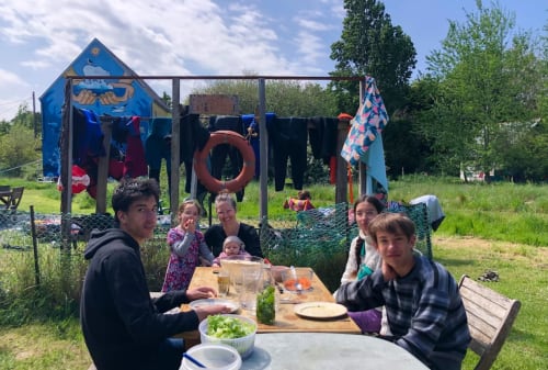 Guests dining outdoors at Le Lama Zébré, a quirky BnB in Penmarch with blue artwork and play structures visible behind the