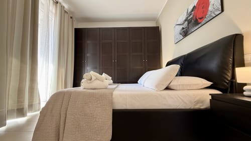 Camera elegante con letto in pelle nera, biancheria color crema, armadio in legno scuro e luce naturale nell'appartamento di Palermo