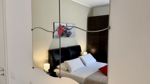 Camera da letto moderna con parete specchiata, letto in metallo nero, biancheria bianca e cuscino rosso in appartamento a Palermo