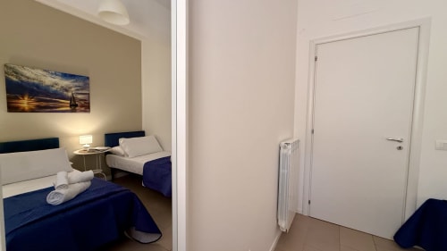 Due letti singoli con coperte blu navy in luminosa camera da letto di appartamento a Palermo, porta bianca e termosifone visibili