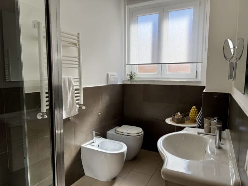 Moderno bagno nell'appartamento di Palermo con bidet, WC, vasca, doppio lavabo, piastrelle scure e finestre con tende a rullo