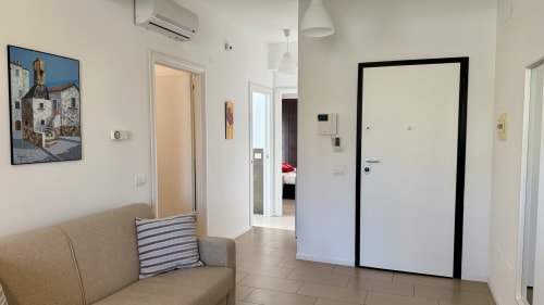 Ingresso di moderno appartamento a Palermo con divano beige, pavimento in piastrelle, pareti bianche e porte che conducono alle camere da letto
