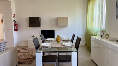 Elegante zona pranzo nell'appartamento di Palermo con tavolo in vetro, sedie nere e vista sulla città attraverso tende verdi