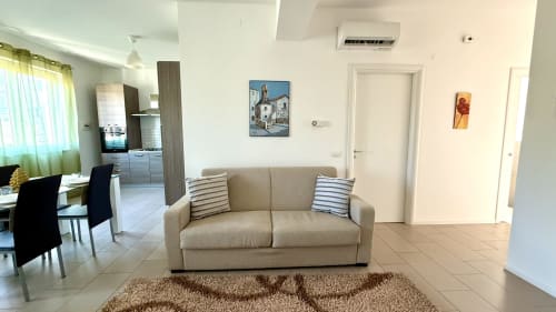 Salotto di appartamento moderno a Palermo con due camere, divano beige, cuscini rigati e vista sulla cucina