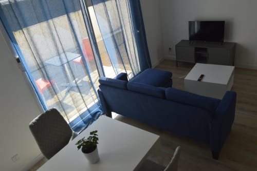 Salon moderne à la Résidence des dunes avec canapé bleu, télévision et vue sur la piscine par les grandes baies vitrées