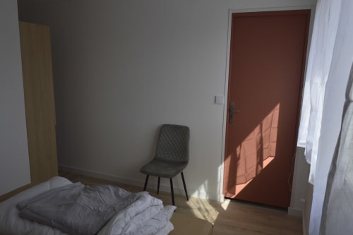 Chambre lumineuse du gîte Résidence des dunes à Landéda avec lit, chaise noire et porte rouge baignée de lumière naturelle