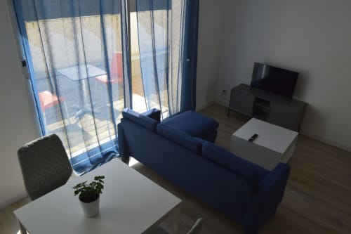 Salon moderne avec canapé bleu, téléviseur et plante à la Résidence des dunes à Landéda, vue piscine par les grandes baies