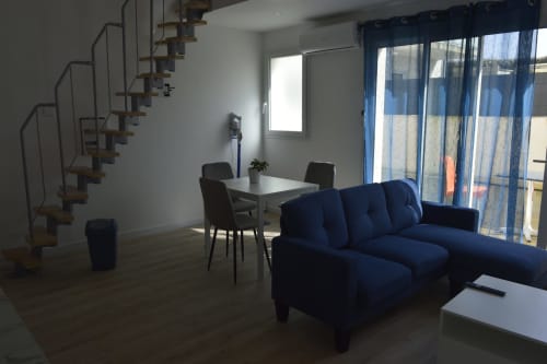 Séjour moderne avec canapé bleu, coin repas et escalier en spirale dans une location de vacances à Landéda