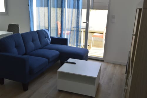 Séjour moderne avec canapé bleu marine, table blanche et portes-fenêtres à la Résidence des dunes à Landéda