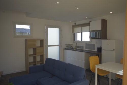 Espace de vie moderne à la Résidence des dunes avec kitchenette, canapé bleu marine et coin repas à Landéda