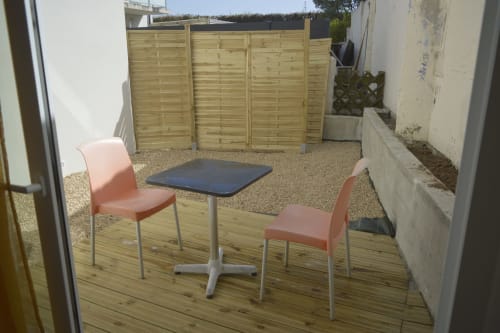 Terrasse extérieure de la cottage Résidence des dunes avec terrasse en bois, deux chaises corail, petite table et clôture de bois